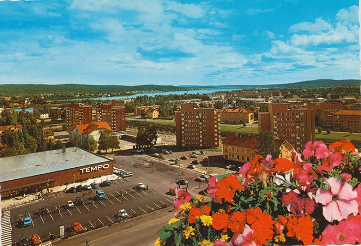 Vykort med bild av en tom parkeringsplats och färgglada blommor