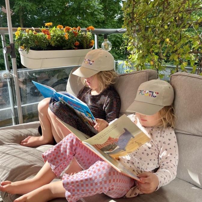 två barn läser böcker med en varsin Postis-keps på huvudet